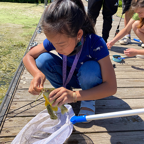 Child kneeling down on a dock putting a worm on the fishing hook