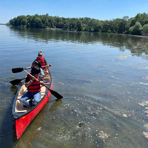 Three kids in a red canoe paddling toward the camera