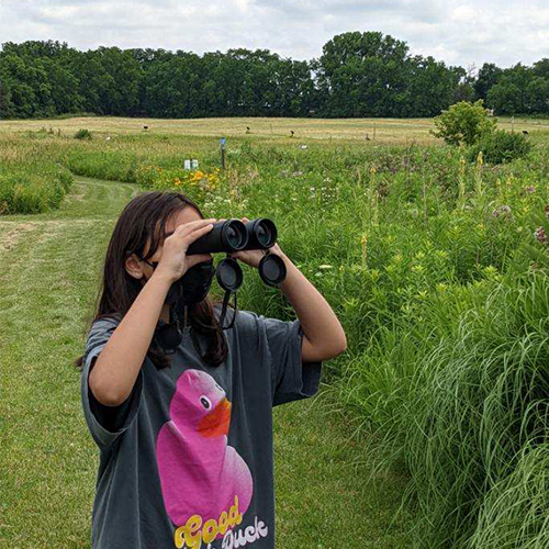 youth standing on a prairie trail looking through binoculars