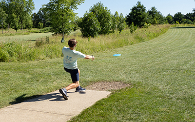 An adult standing on a disc golf tee throwing a disc 