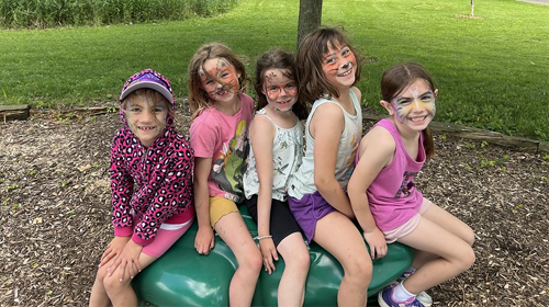 Five kids with painted faces sitting on a rock smiling at the camera